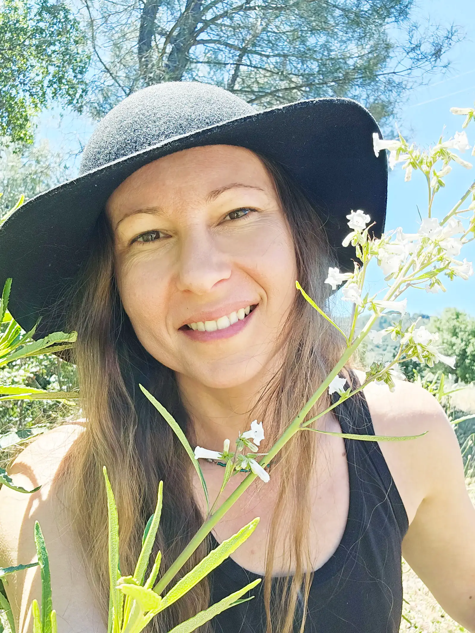 Whittney, founder of Medicinal Herbarium, outdoors wearing a wide-brimmed hat among white wildflowers